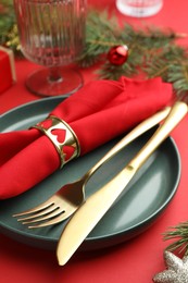 Photo of Beautiful Christmas setting with plate, elegant cutlery and festive decor on red table