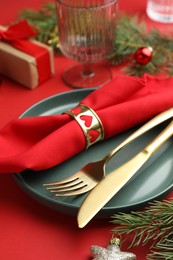 Photo of Beautiful Christmas setting with plate, elegant cutlery and festive decor on red table