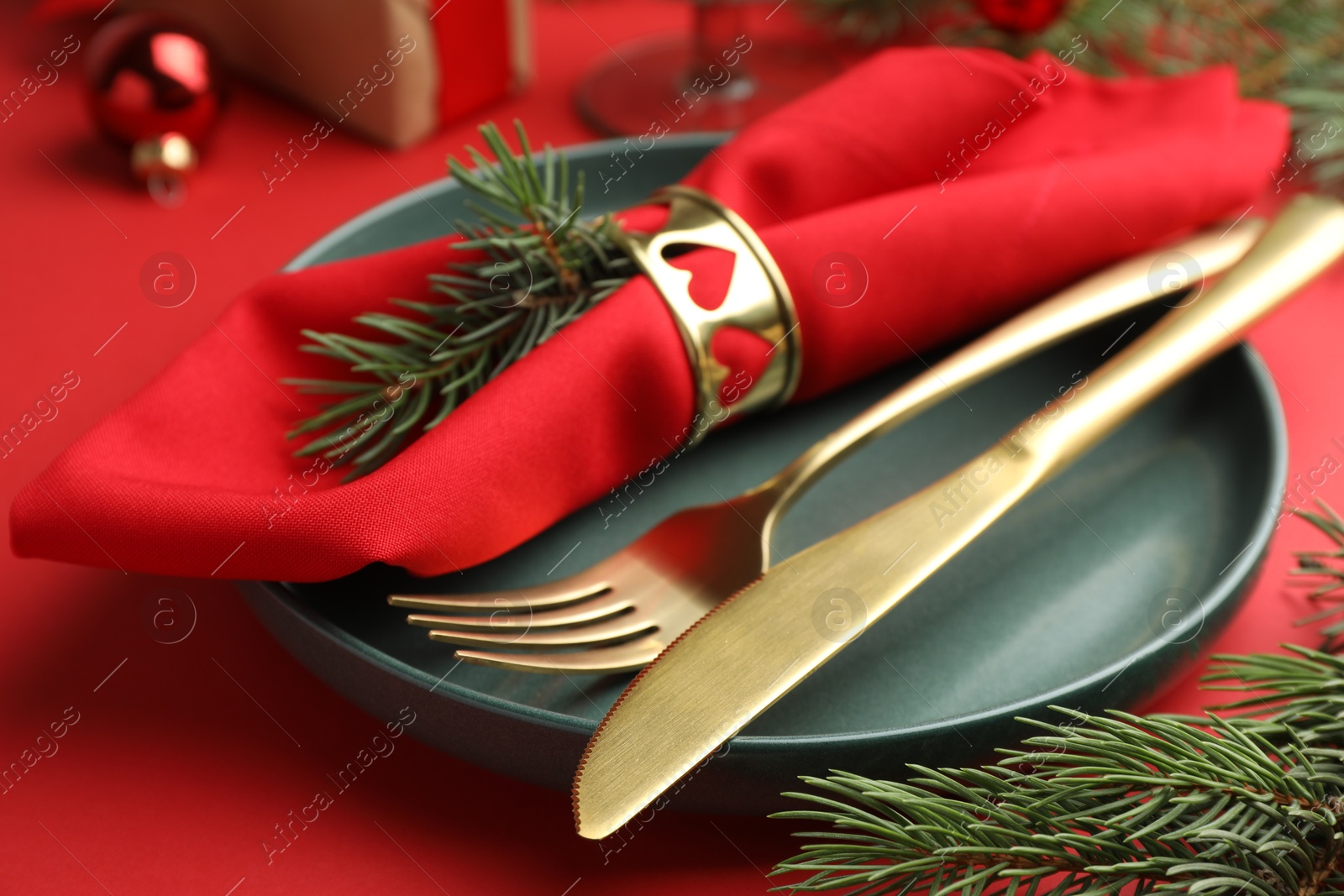 Photo of Beautiful Christmas setting with plate, elegant cutlery and festive decor on red table, closeup