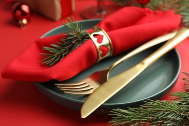 Photo of Beautiful Christmas setting with plate, elegant cutlery and festive decor on red table, closeup