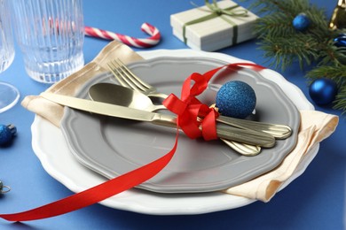 Photo of Beautiful Christmas setting with plates, elegant cutlery and festive decor on blue table, closeup