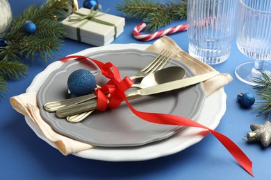 Photo of Beautiful Christmas setting with plates, elegant cutlery and festive decor on blue table, closeup