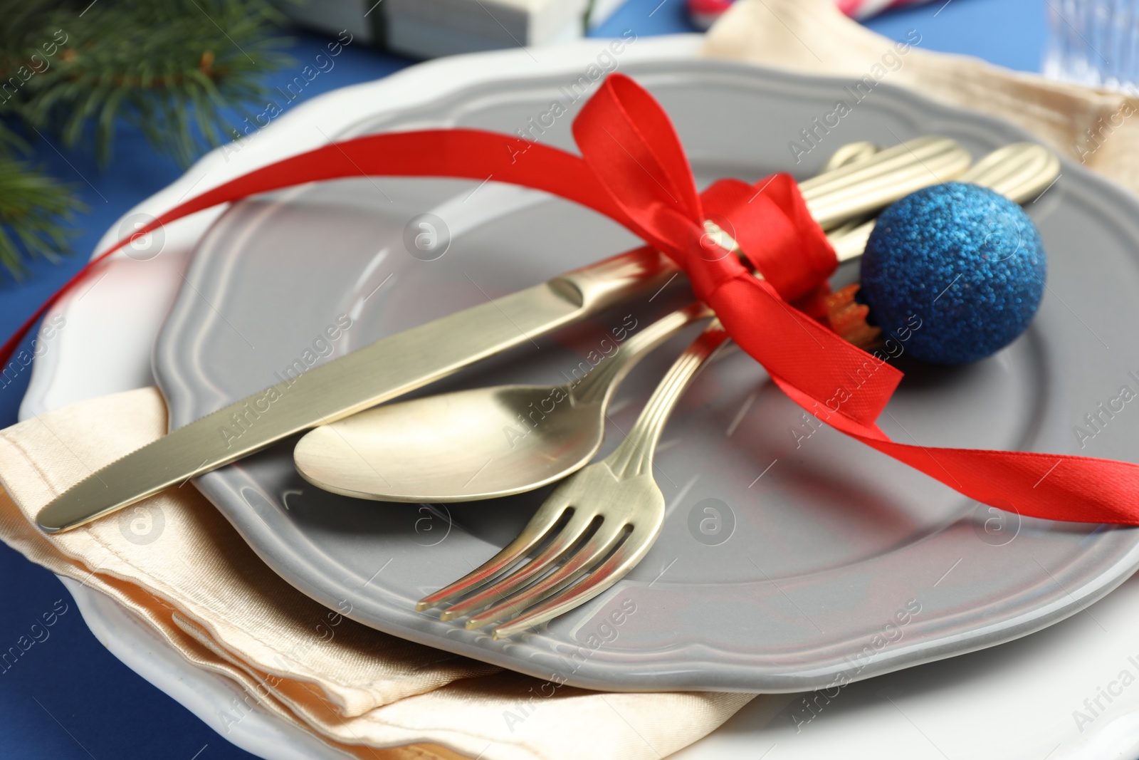 Photo of Beautiful Christmas setting with plates, elegant cutlery and festive decor on blue table, closeup