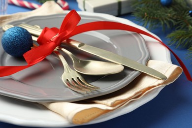 Photo of Beautiful Christmas setting with plates, elegant cutlery and festive decor on blue table, closeup