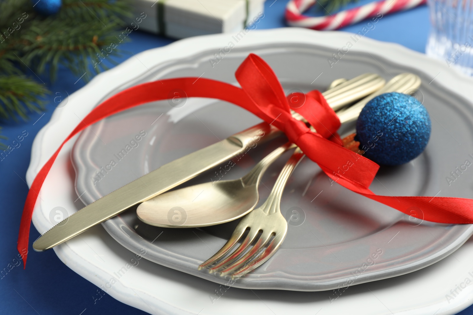 Photo of Beautiful Christmas setting with plates, elegant cutlery and festive decor on blue table, closeup