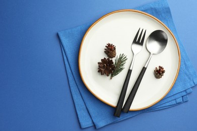 Photo of Beautiful Christmas setting with plate, cutlery and cones on blue table, top view