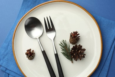 Photo of Beautiful Christmas setting with plate, cutlery and cones on blue table, top view