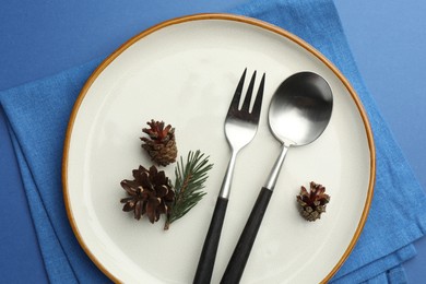 Photo of Beautiful Christmas setting with plate, cutlery and cones on blue table, top view