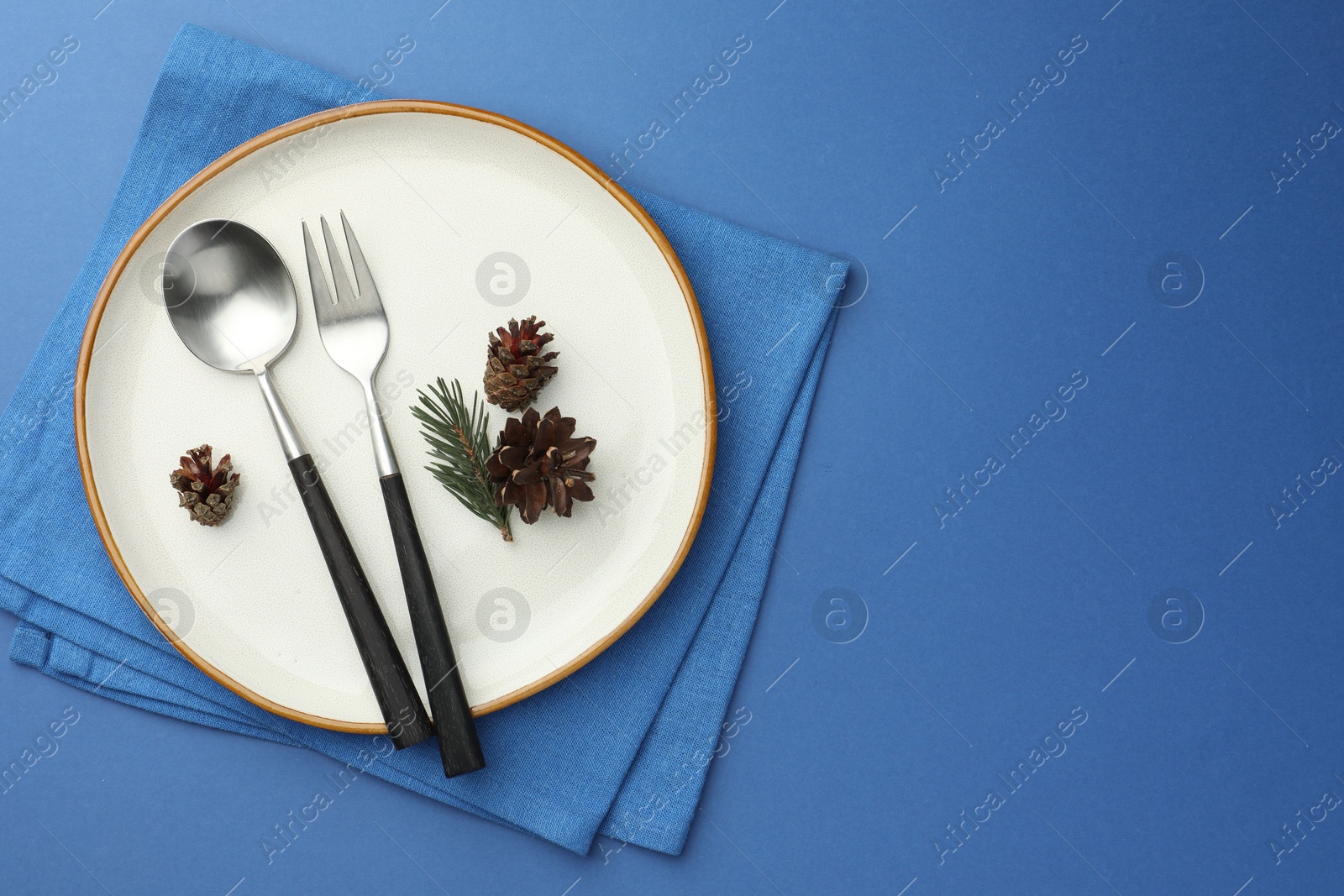 Photo of Beautiful Christmas setting with plate, cutlery and cones on blue table, top view. Space for text