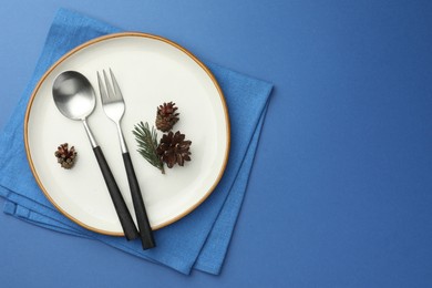 Photo of Beautiful Christmas setting with plate, cutlery and cones on blue table, top view. Space for text