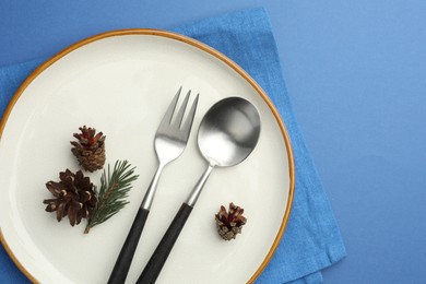 Photo of Beautiful Christmas setting with plate, cutlery and cones on blue table, top view