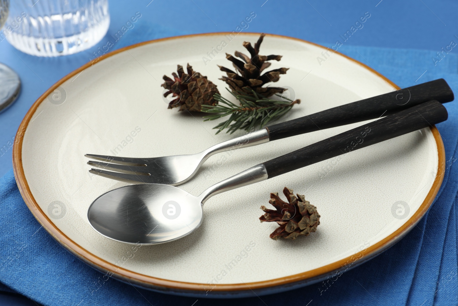 Photo of Beautiful Christmas setting with plate, cutlery and cones on blue table