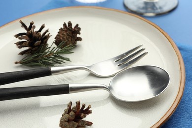 Photo of Beautiful Christmas setting with plate, cutlery and cones on blue table, closeup