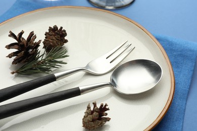 Photo of Beautiful Christmas setting with plate, cutlery and cones on blue table, closeup