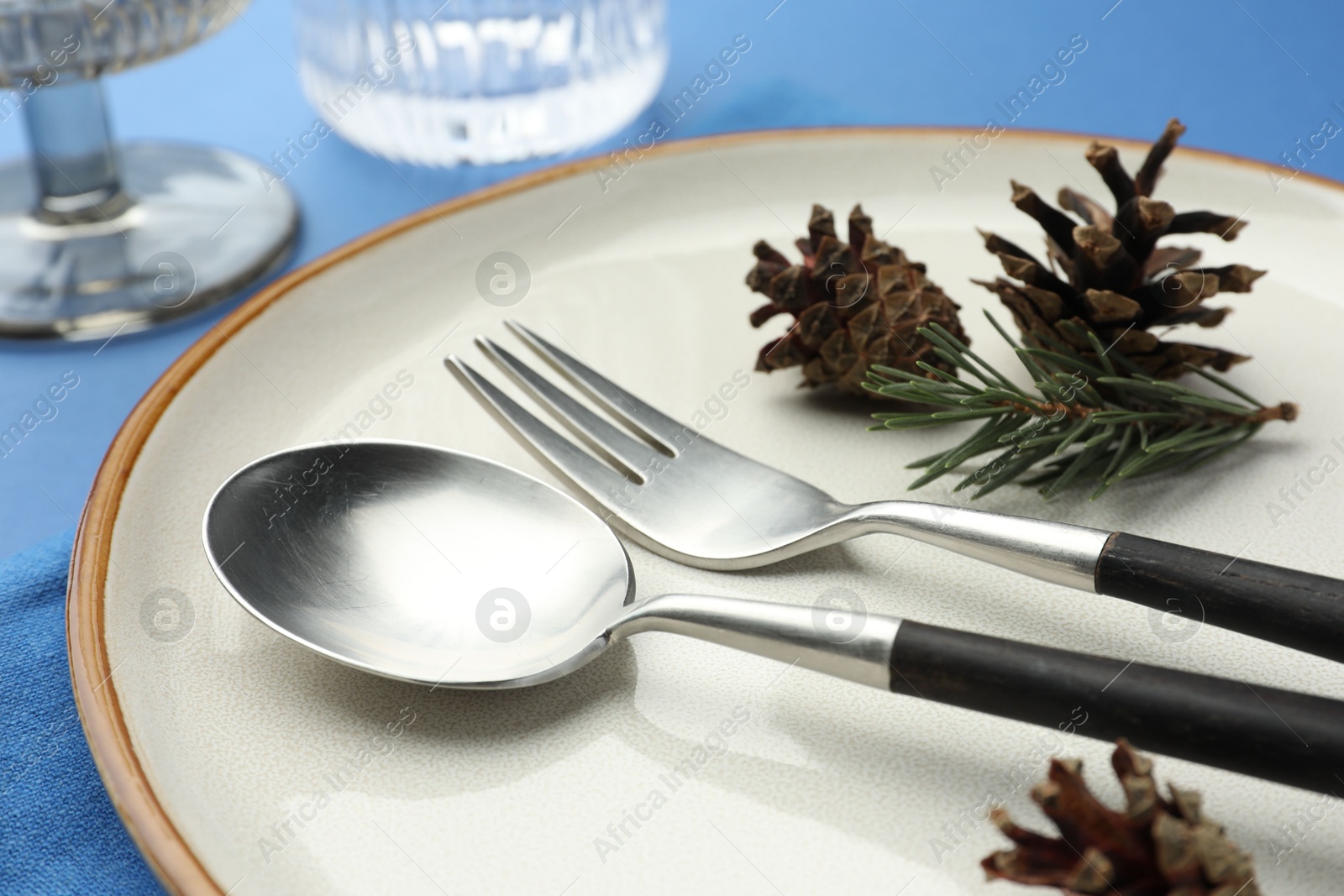 Photo of Beautiful Christmas setting with plate, cutlery and cones on blue table, closeup