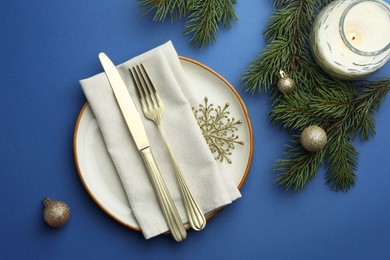 Photo of Beautiful Christmas setting with plate, elegant cutlery and festive decor on blue table, flat lay