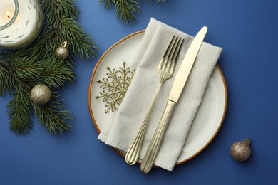 Photo of Beautiful Christmas setting with plate, elegant cutlery and festive decor on blue table, flat lay