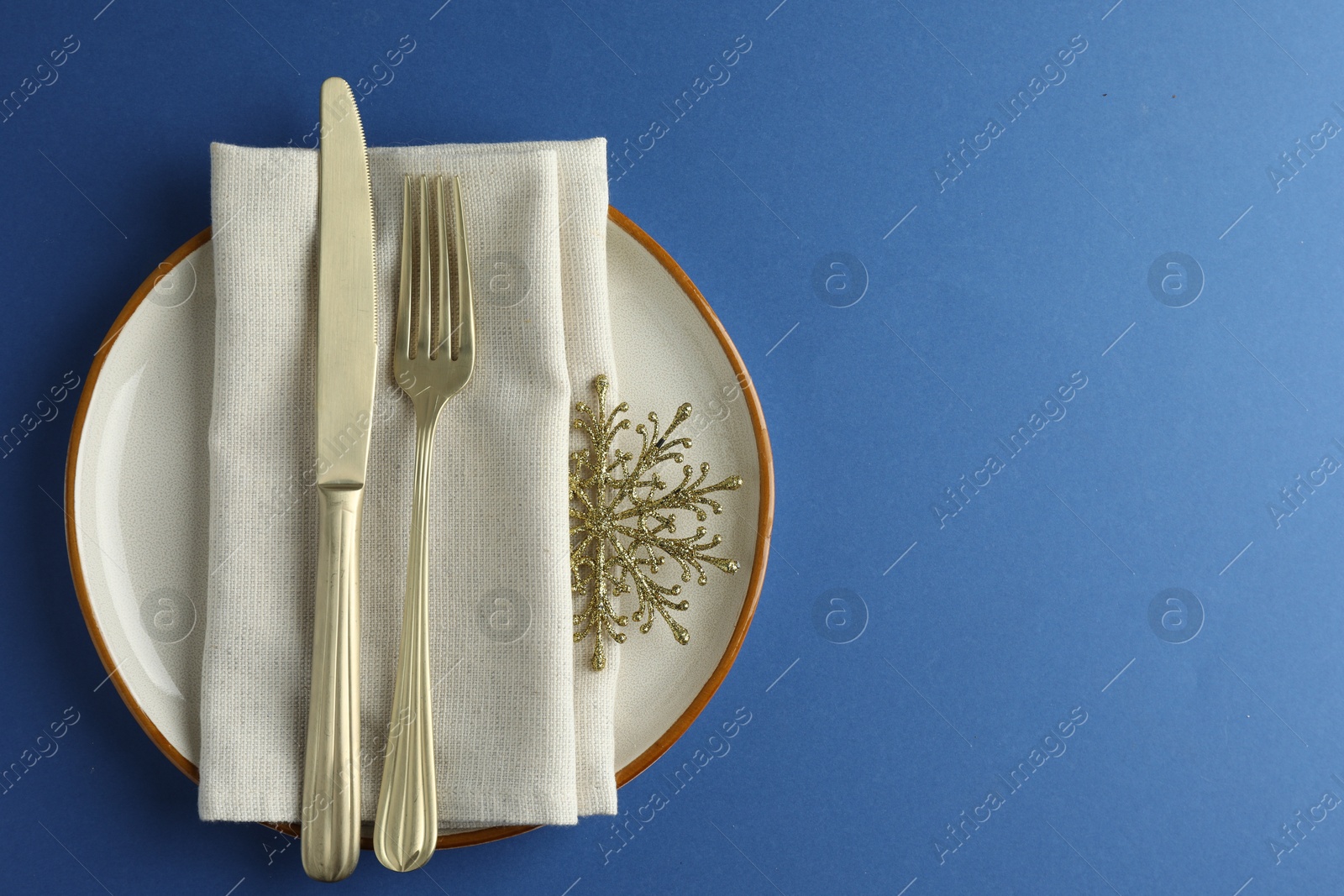 Photo of Beautiful Christmas setting with plate, elegant cutlery and golden snowflake on blue table, top view. Space for text