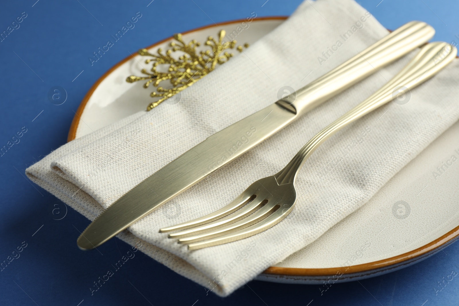 Photo of Beautiful Christmas setting with plate, elegant cutlery and golden snowflake on blue table, closeup