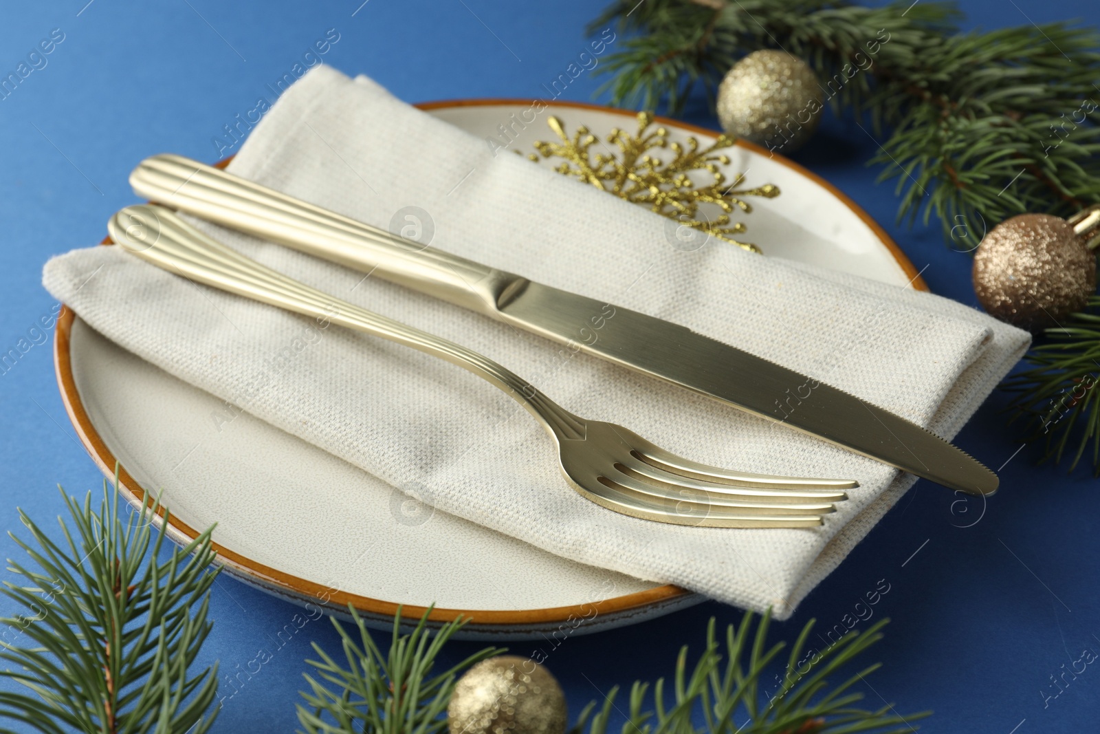 Photo of Beautiful Christmas setting with plate, elegant cutlery and festive decor on blue table, closeup