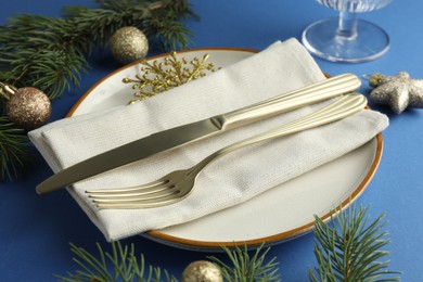 Photo of Beautiful Christmas setting with plate, elegant cutlery and festive decor on blue table, closeup