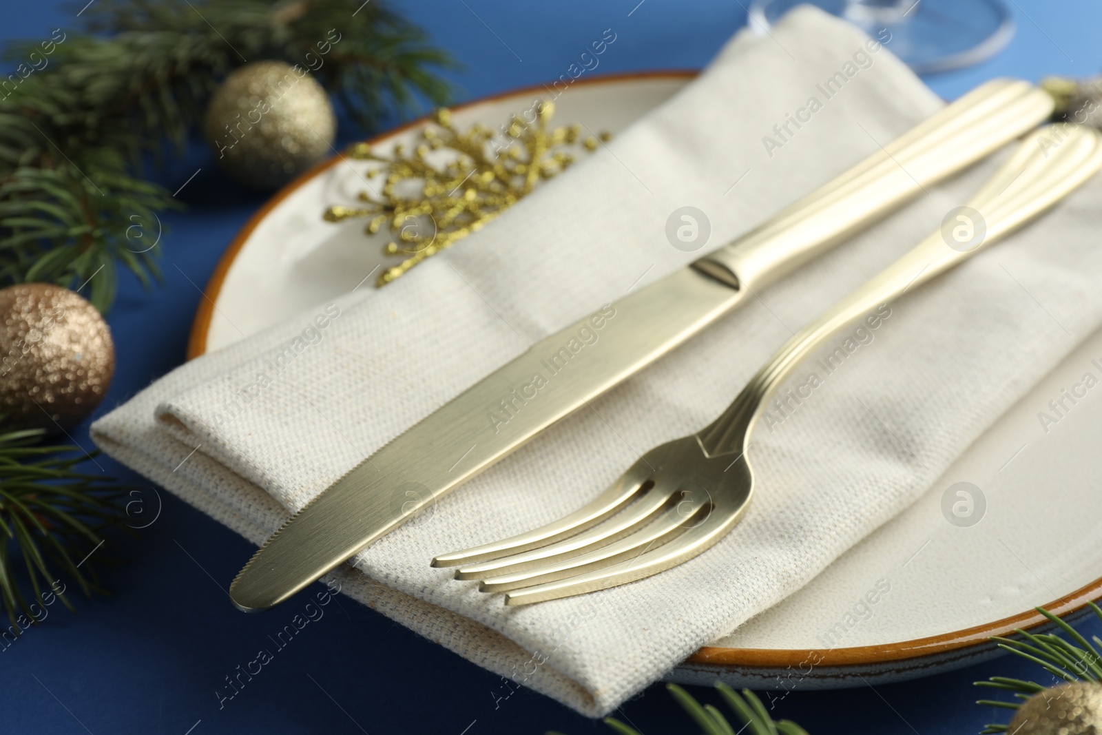 Photo of Beautiful Christmas setting with plate, elegant cutlery and festive decor on blue table, closeup