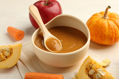 Photo of Delicious baby food with spoon in bowl and fresh ingredients on white wooden table