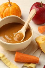 Photo of Delicious baby food with spoon in bowl and fresh ingredients on white wooden table