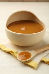 Photo of Delicious baby food in bowl and spoon on white wooden table