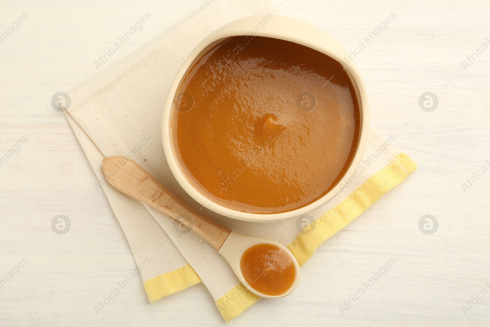 Photo of Delicious baby food in bowl and spoon on white wooden table, flat lay