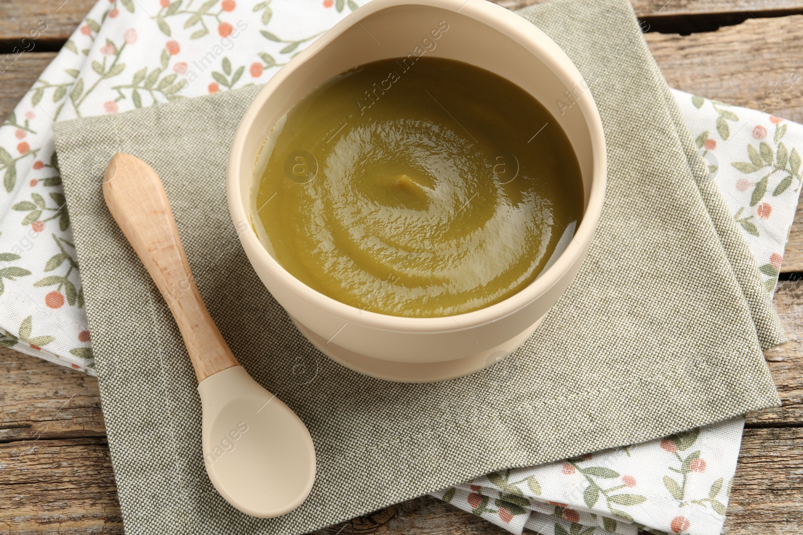 Photo of Delicious baby food in bowl with spoon on wooden table