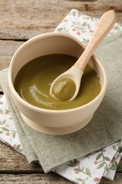 Photo of Delicious baby food in bowl with spoon on wooden table