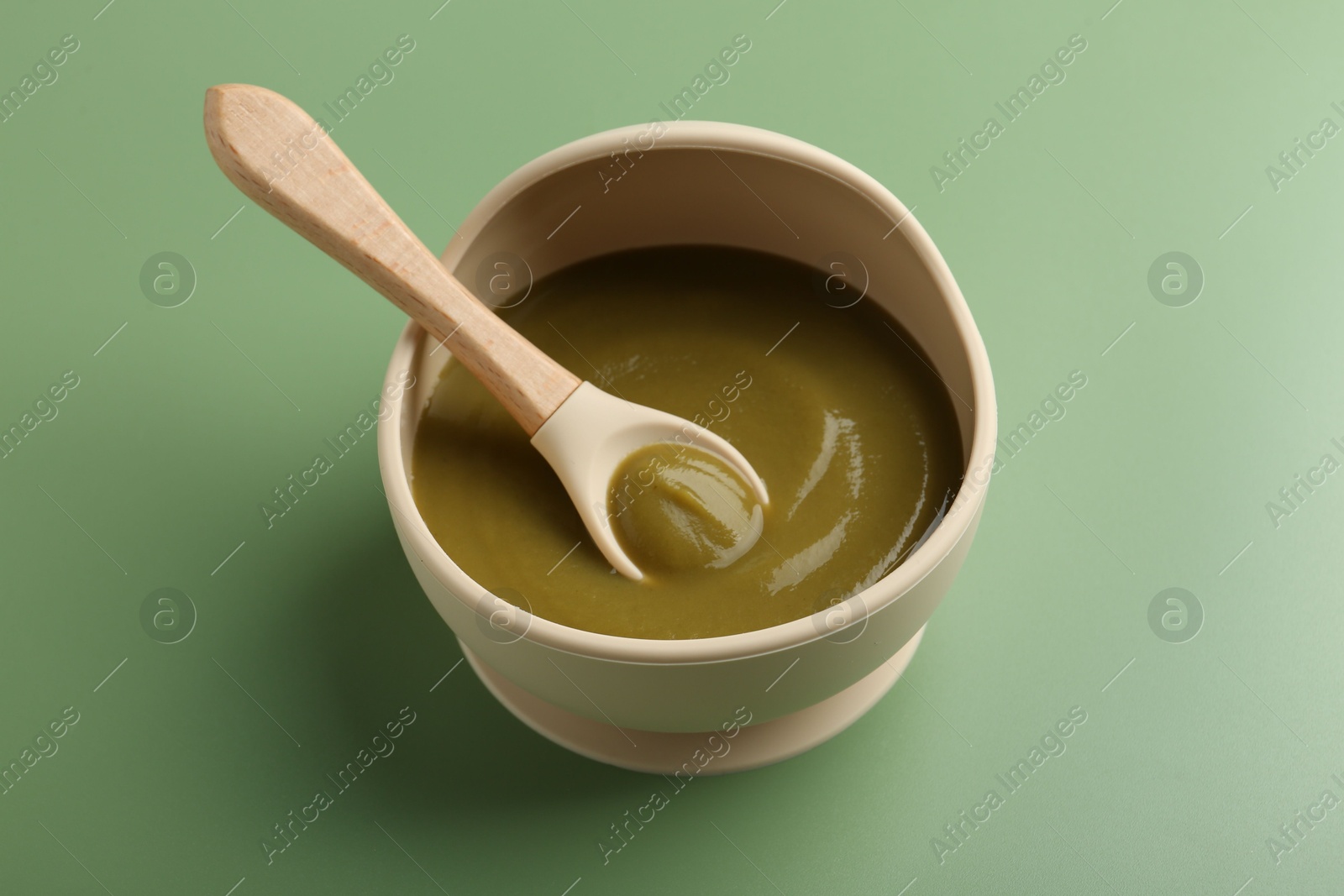 Photo of Delicious baby food with spoon in bowl on green table