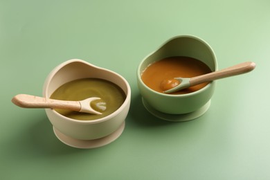 Photo of Delicious baby food with spoons in bowls on green table