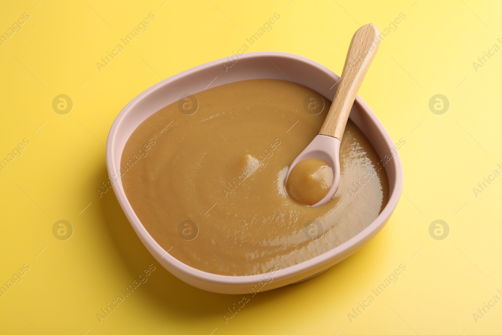 Photo of Delicious baby food with spoon in bowl on yellow table