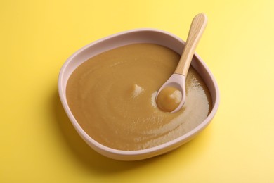 Photo of Delicious baby food with spoon in bowl on yellow table