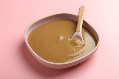 Photo of Delicious baby food with spoon in bowl on pink table