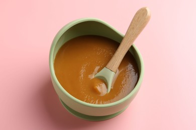 Photo of Delicious baby food with spoon in bowl on pink table