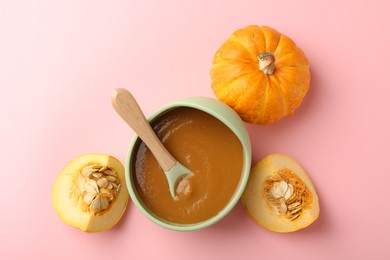 Photo of Delicious baby food with spoon in bowl and fresh pumpkins on pink table, flat lay