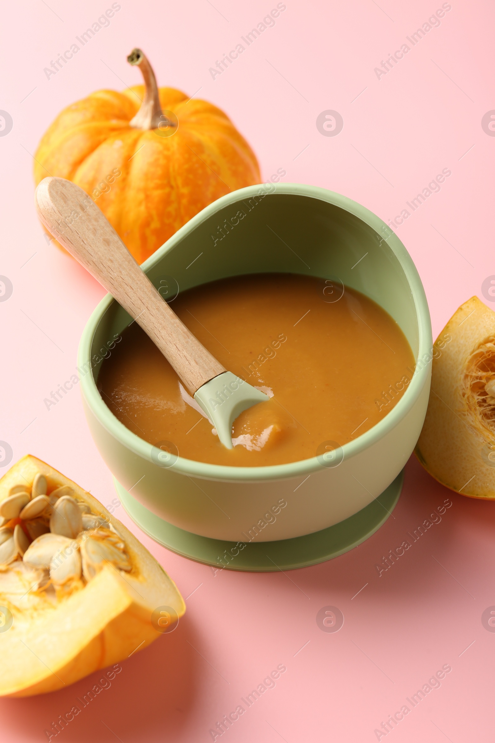 Photo of Delicious baby food with spoon in bowl and fresh pumpkins on pink table