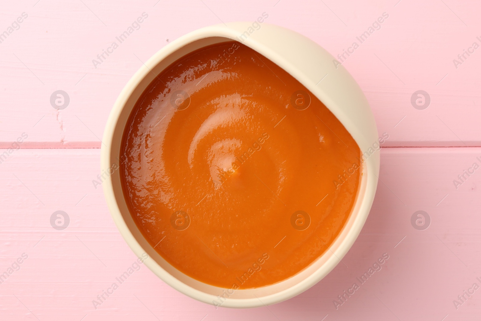 Photo of Delicious baby food in bowl on pink wooden table, top view