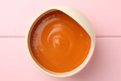 Photo of Delicious baby food in bowl on pink wooden table, top view