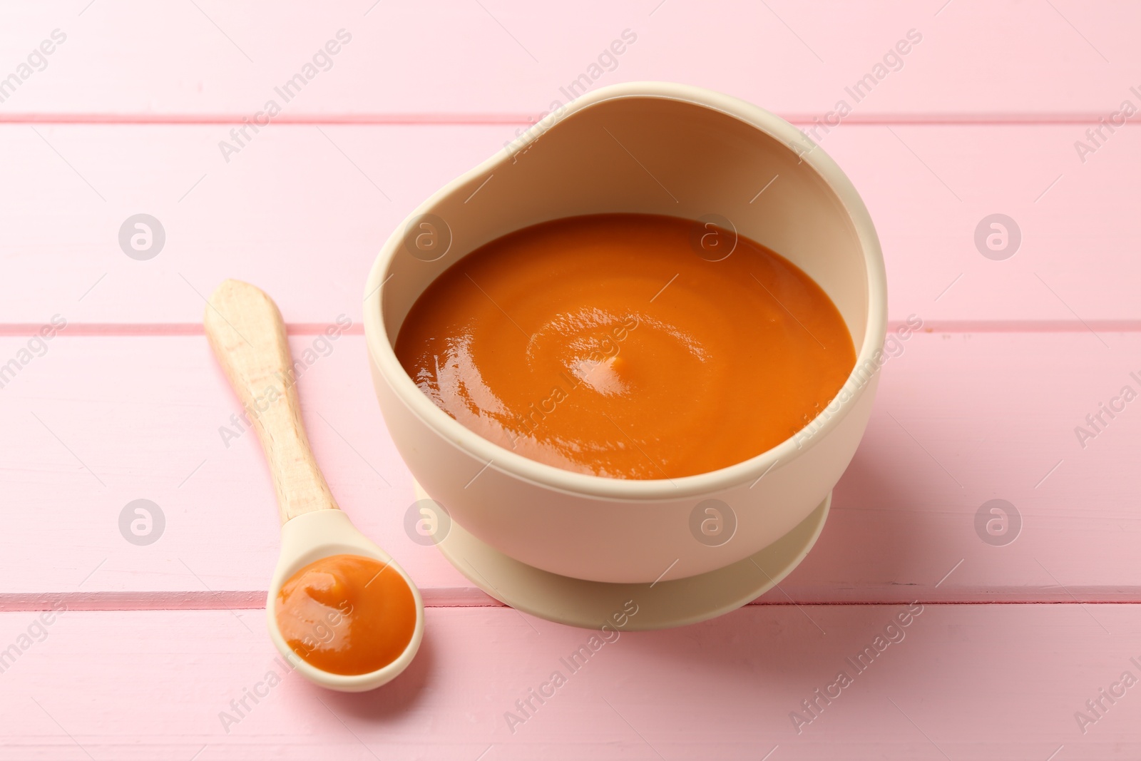 Photo of Delicious baby food in bowl and spoon on pink wooden table