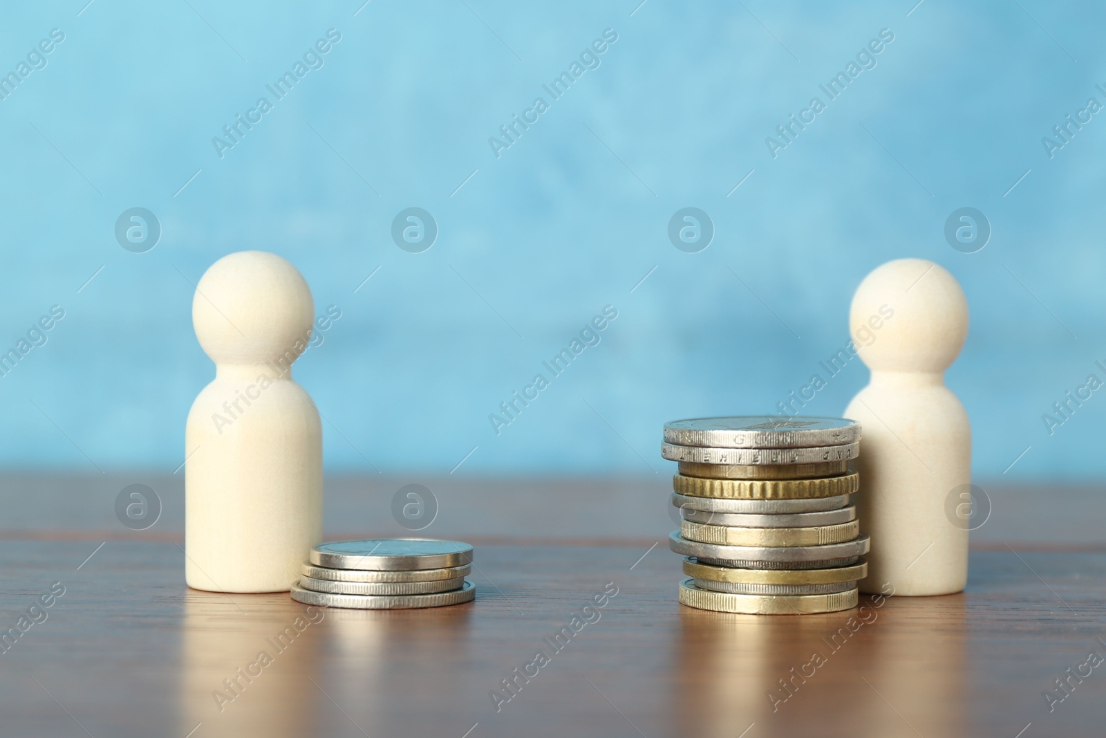 Photo of Financial inequality. Stacks of coins and wooden figures on table against light blue background