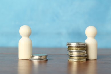 Financial inequality. Stacks of coins and wooden figures on table against light blue background