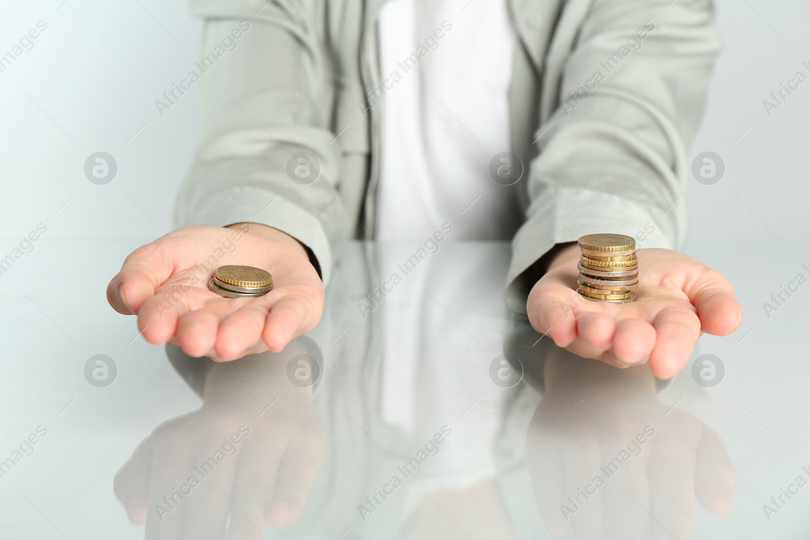 Photo of Financial inequality. Woman comparing two stacks of coins at table, closeup