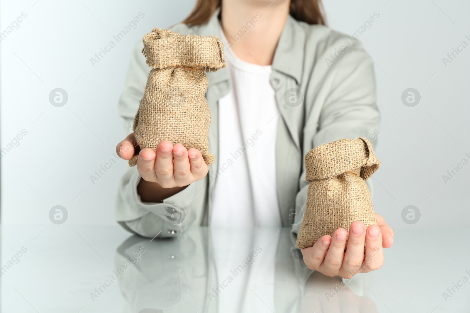 Photo of Financial inequality. Woman comparing two sacks in hands at white table, closeup