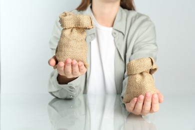 Financial inequality. Woman comparing two sacks in hands at white table, closeup