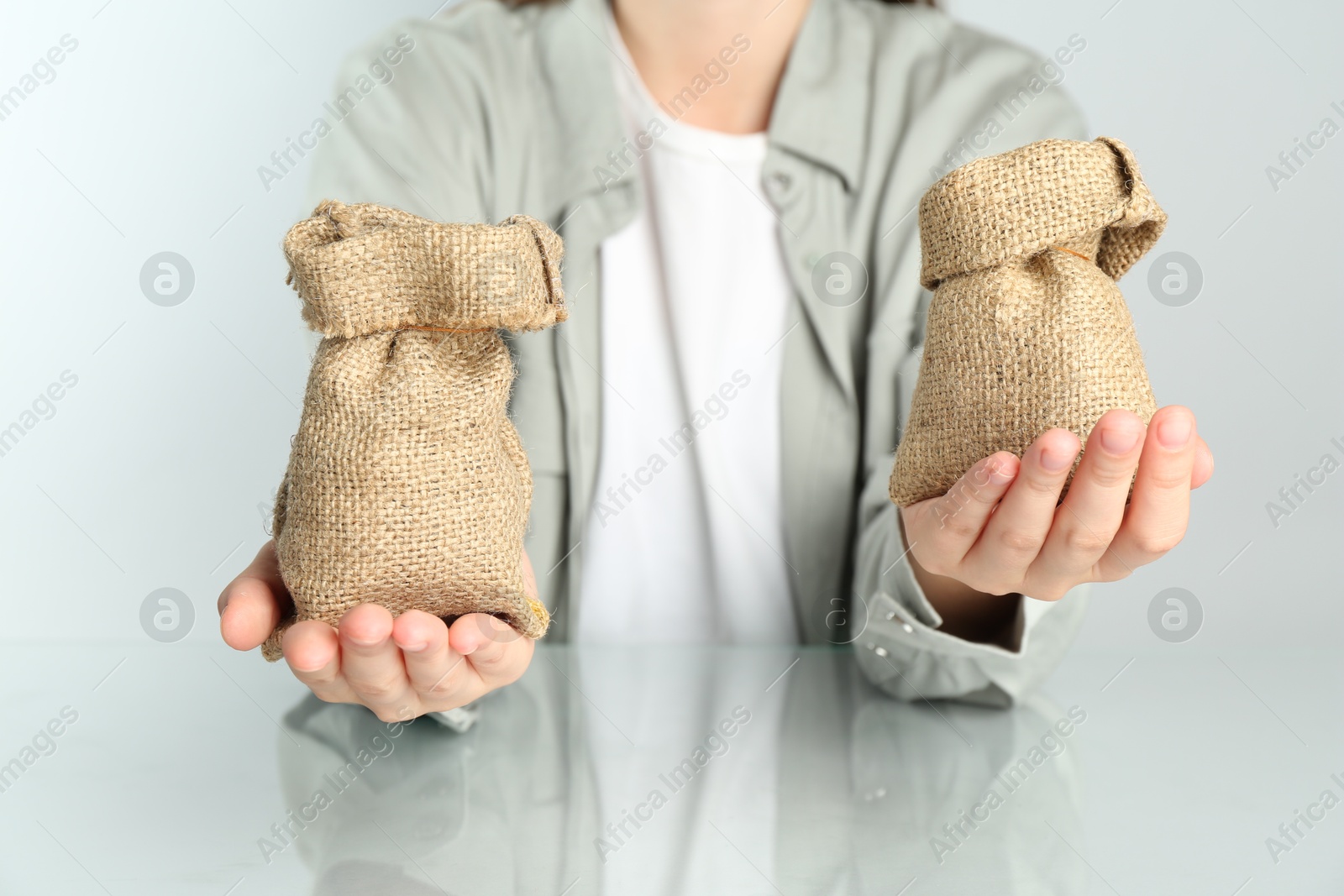 Photo of Financial inequality. Woman comparing two sacks in hands at white table, closeup