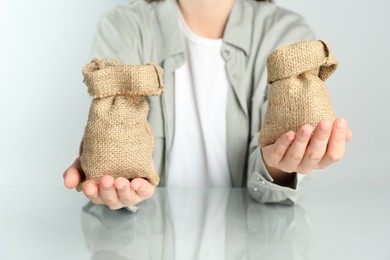 Photo of Financial inequality. Woman comparing two sacks in hands at white table, closeup